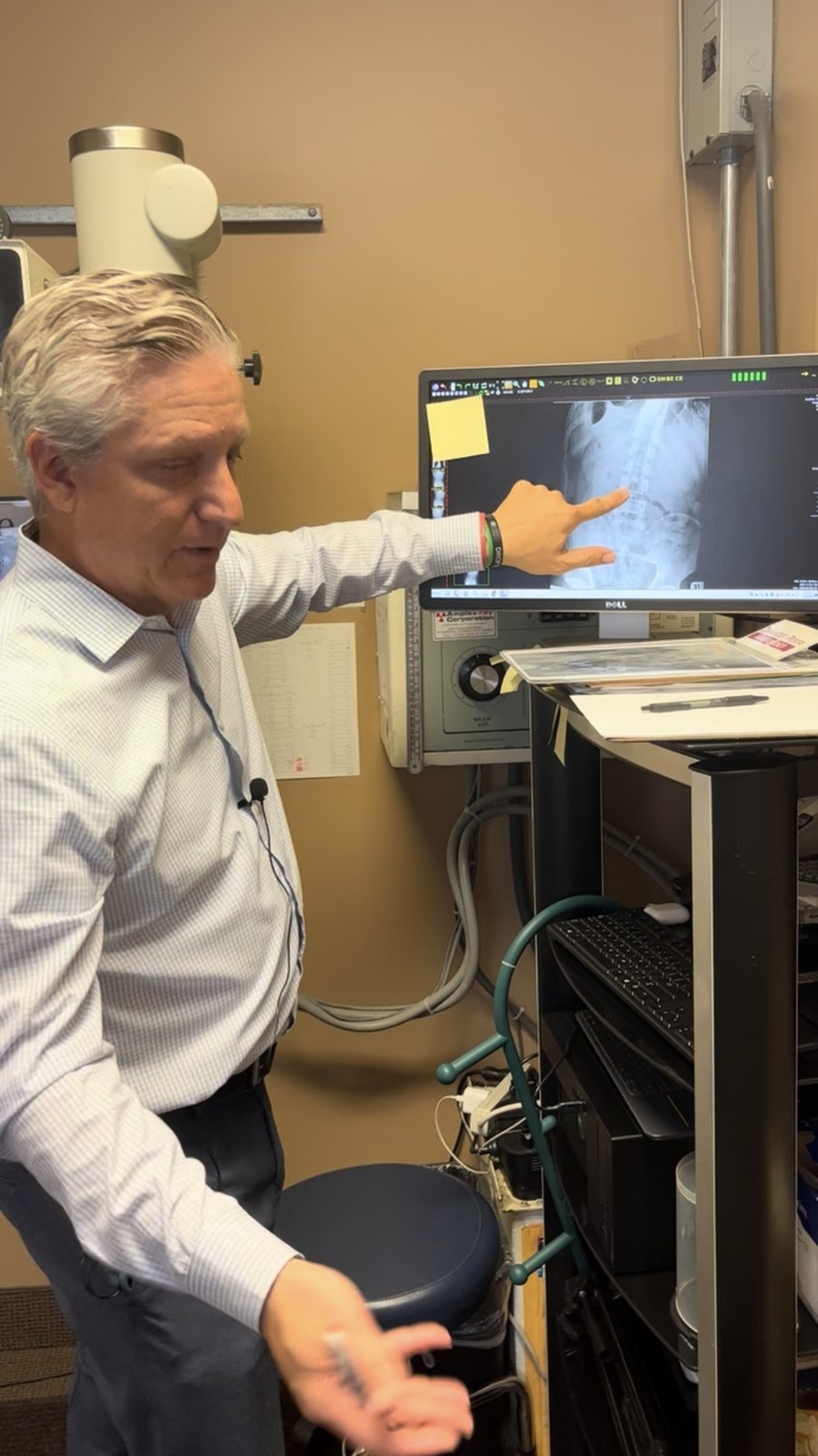 Dr. Chris Hansen pointing to a patient's spinal x-ray on screen while explaining the findings, at Hansen Chiropractic in West Babylon